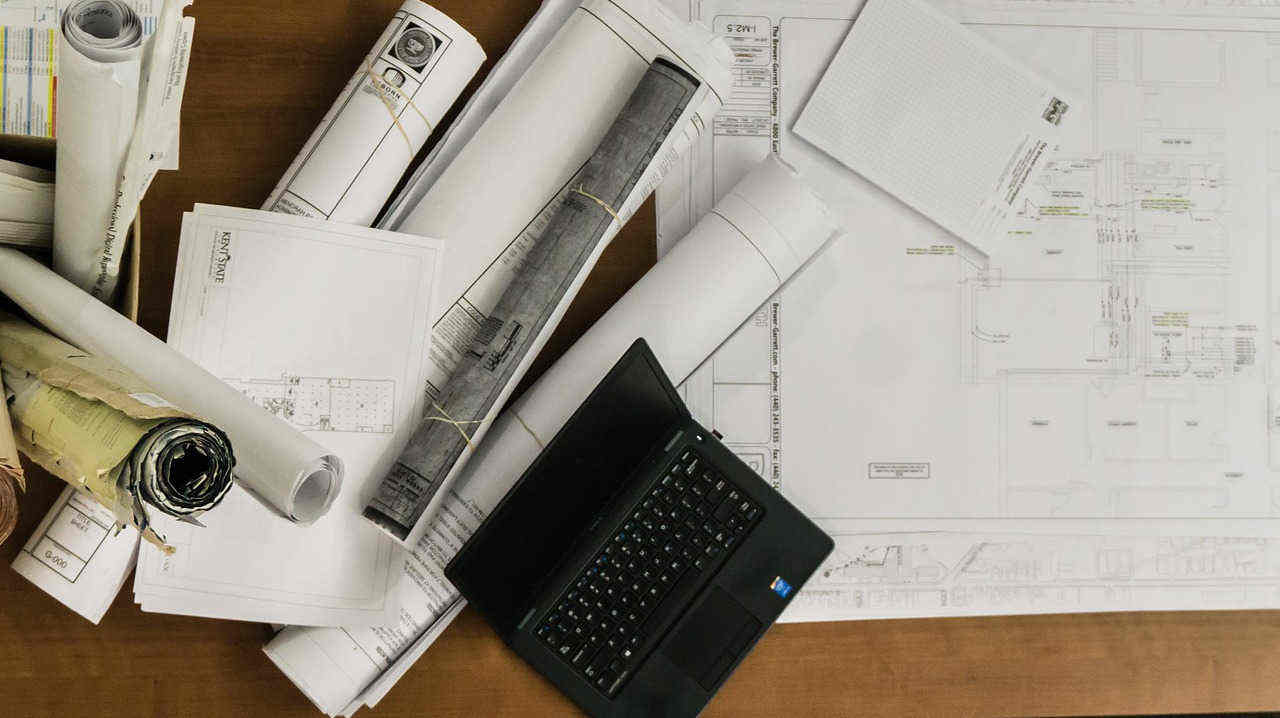 Architektonické plány na stole s notebookem - symbolizující strategické plánování projektů